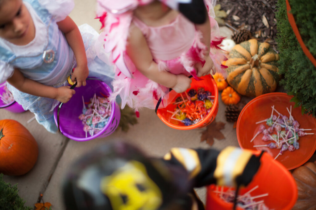 Children in Halloween costumes carrying buckets filled with candy while trick-or-treating.